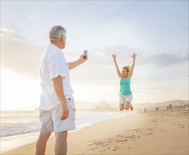 Caucasian man taking cell phone photograph of wife on beach