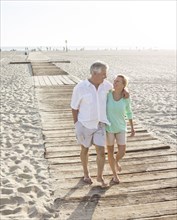Caucasian couple walking on wooden boardwalk on beach