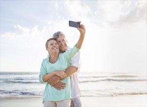 Caucasian couple taking cell phone selfie on beach