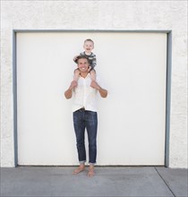 Caucasian father holding son on shoulders in driveway