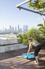 Older mixed race woman spreading yoga mat on urban rooftop