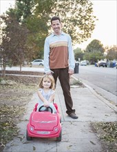 Caucasian father pushing daughter in toy car