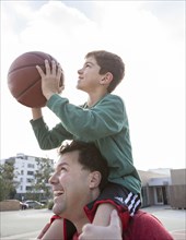 Caucasian father carrying son with basketball on shoulders