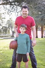 Caucasian father and son smiling in park with basketball