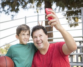 Caucasian father and son taking cell phone photograph on bleachers
