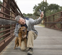 Caucasian man taking photograph with dog on bridge