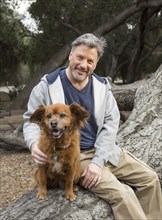 Caucasian man and dog sitting on tree in park