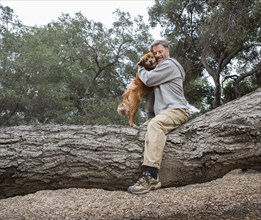 Caucasian man hugging dog on tree in park