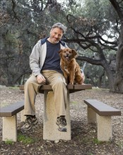 Caucasian man and dog sitting on picnic table in park