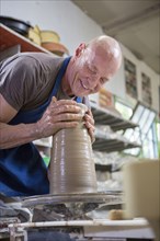 Older Caucasian man forming pottery on wheel in ceramics studio