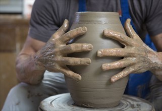 Older Caucasian man forming pottery on wheel in ceramics studio