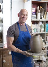 Proud older Caucasian man holding pottery in ceramics studio