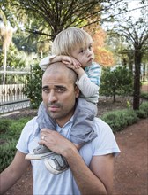 Hispanic father carrying son on shoulders in park