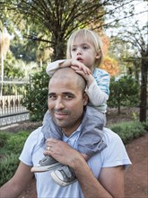 Hispanic father carrying son on shoulders in park