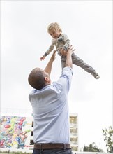 Hispanic father throwing son in air outdoors