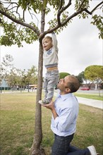 Hispanic father and son playing on tree in park