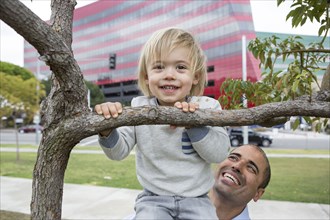 Hispanic father and son playing on tree in park