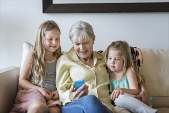 Caucasian grandmother and granddaughters using cell phone on sofa