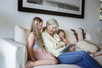 Caucasian grandmother and granddaughters using digital tablet on sofa