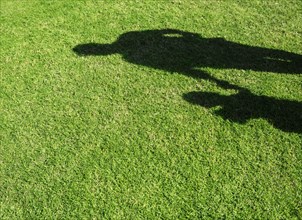 Shadow of Hispanic father and son on grass lawn