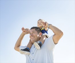 Low angle view of Hispanic father carrying son on shoulders
