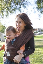 Hispanic mother wearing son in carrier in park