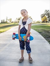 Mixed race girl holding skateboard in park