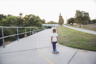 Mixed race girl riding skateboard in park