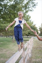 Father helping daughter balance on wooden fence