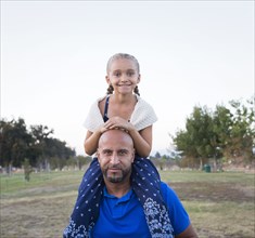 Father carrying daughter on shoulders in park