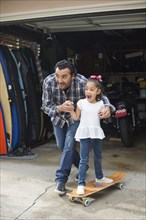 Hispanic father teaching daughter to ride skateboard