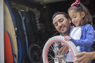 Hispanic father teaching daughter to repair bicycle