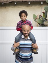 Mixed race father carrying son on shoulders