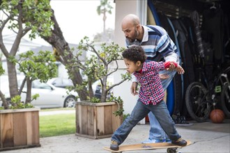 Mixed race father teaching son to ride skateboard outdoors