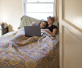 Caucasian lesbian couple watching laptop in bed