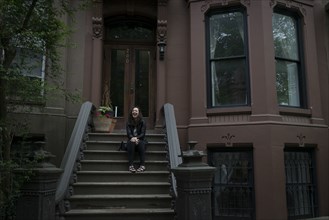 Caucasian woman sitting on townhouse front stoop