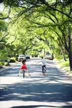 Caucasian children riding bicycles on suburban neighborhood street