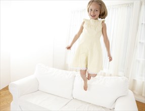 Caucasian girl jumping on sofa in living room