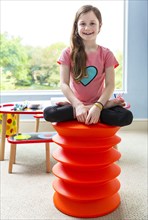 Caucasian girl sitting cross-legged on stool in playroom