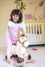 Girl riding rocking horse in nursery