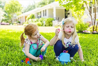 Caucasian sisters blowing bubbles in backyard