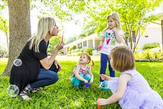 Caucasian mother and daughters blowing bubbles in backyard