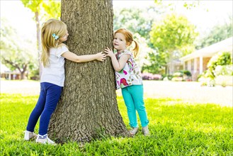 Caucasian sisters hugging tree in backyard