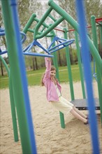 Caucasian girl hanging from structure in playground