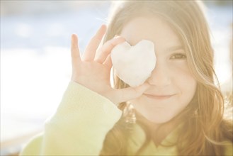 Caucasian girl covering eye with heart shape