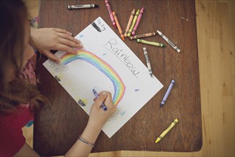 Caucasian girl drawing rainbow with crayons on table