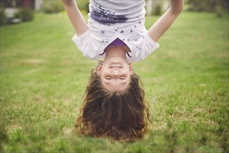 Caucasian girl hanging upside down in backyard