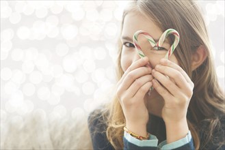 Caucasian girl looking through heart-shape with candy canes