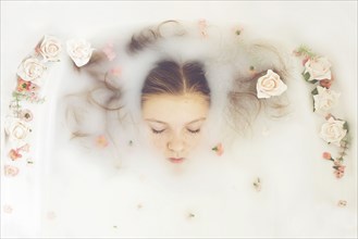 Caucasian teenage girl floating in milk bath with flowers
