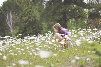 Caucasian girl crouching in field of flowers